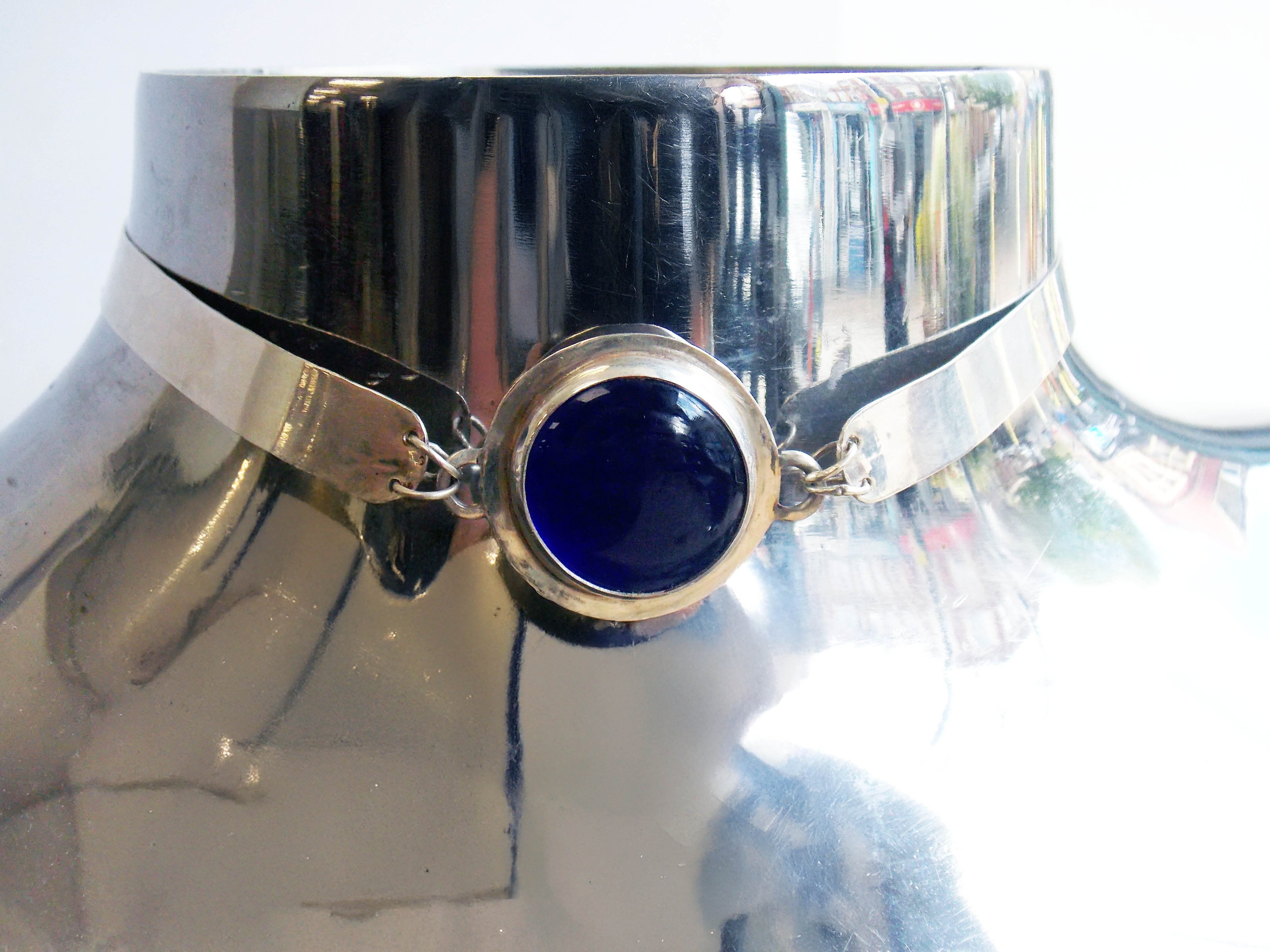 Blue glass cabochon set into a silver choker. The jewellery sits on a chrome bust.