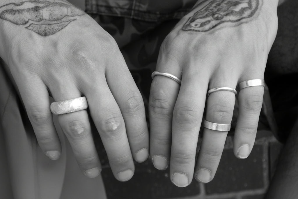 Close-up of two sets of hands with silver rings on fingers against a blurred brick background.