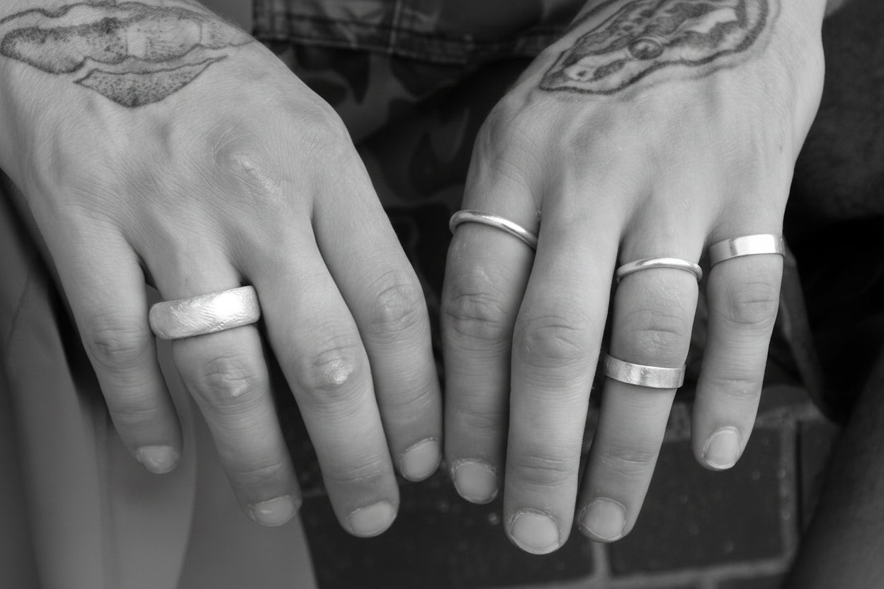 Close-up of two sets of hands with silver rings on fingers against a blurred brick background.