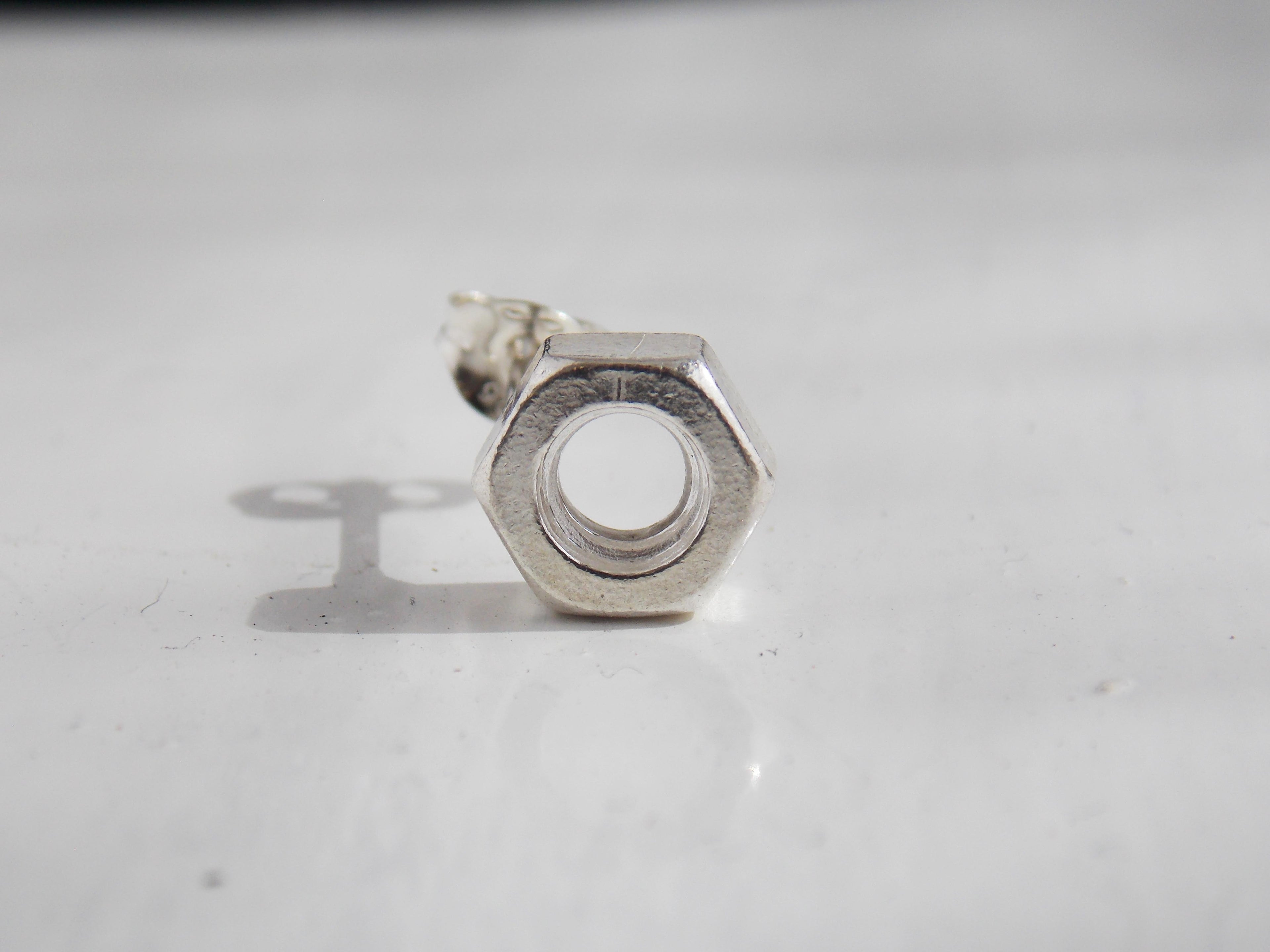 A solid silver nut earring sits on a white background