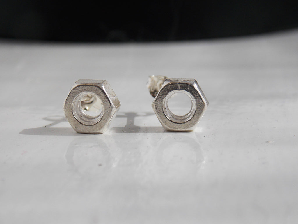 A pair of solid silver nuts as earrings sit on a reflective white background