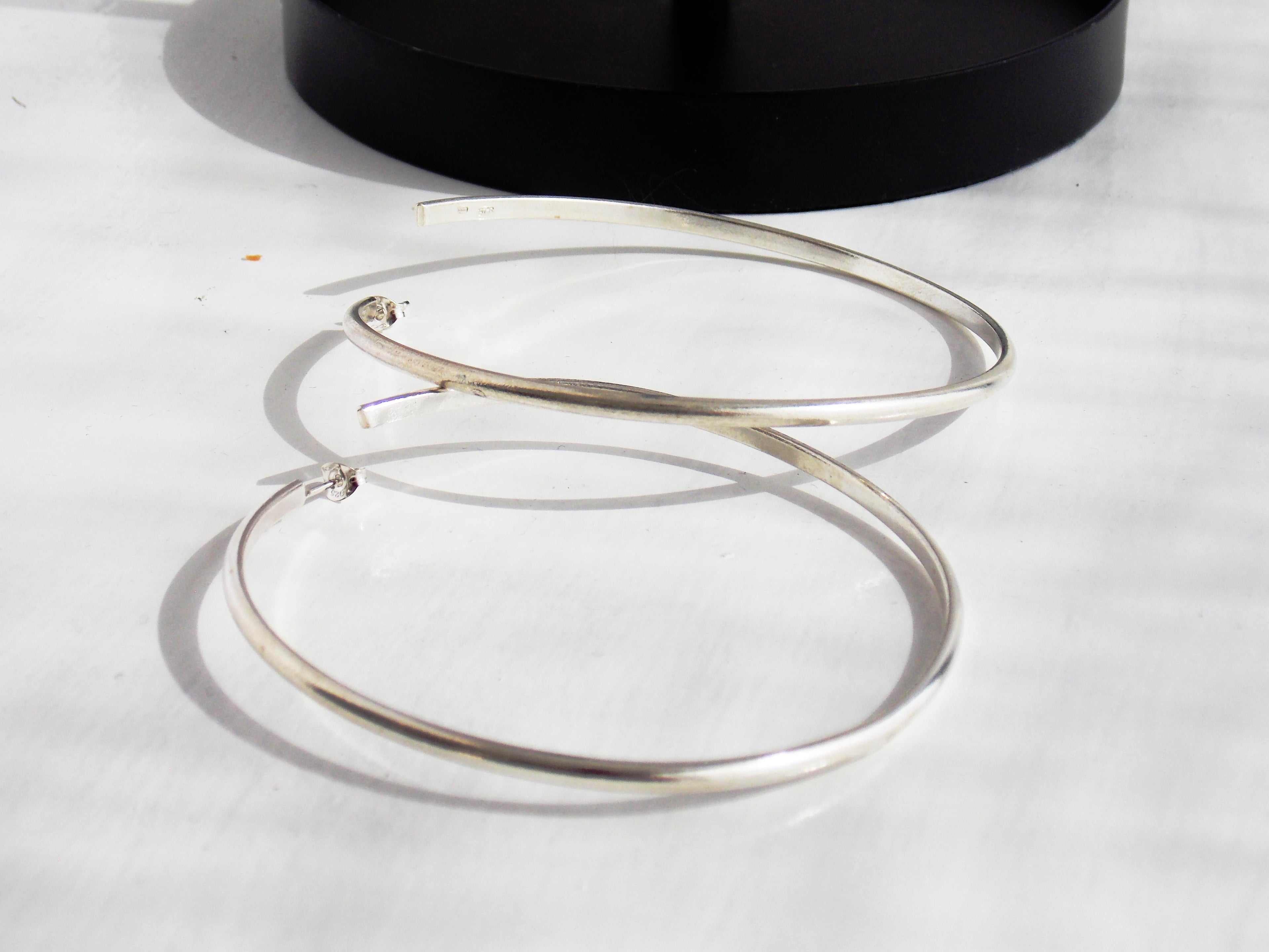 Silver hoop earrings on a light gray surface with a black circular object in the background.