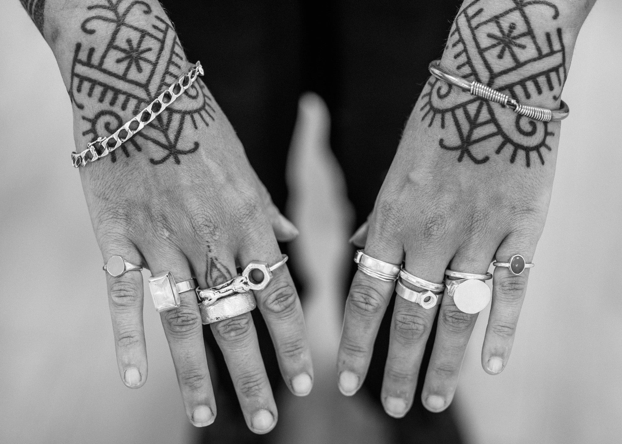 Black and white photo of hands with tattoos and multiple rings.